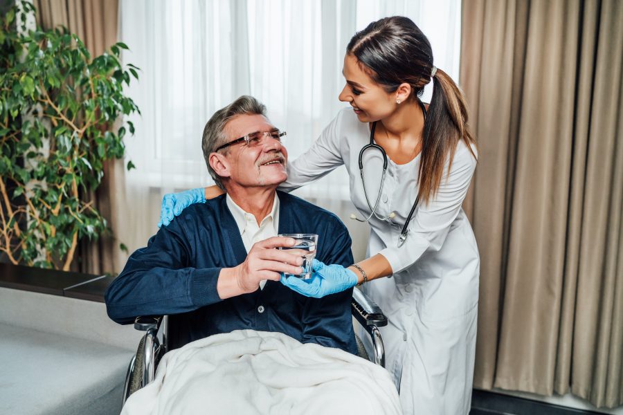 older man wheelchair smiles nurse assistant she hands him glass water