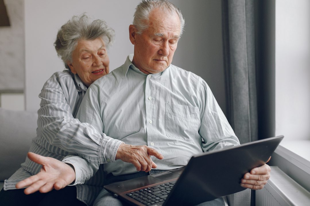 elegantes altes ehepaar das zu hause sitzt und einen laptop benutzt